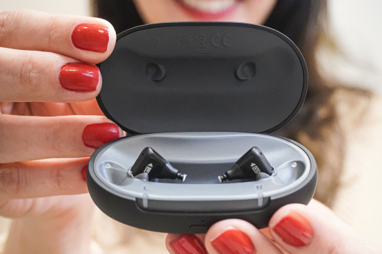 Imagem de uma mulher segurando um aparelho auditivo.