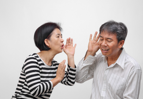 Mulher falando alto para um homem que parece ter dificuldades auditivas.