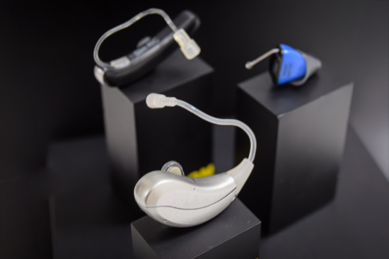 Modelos de aparelhos auditivos modernos sobre base preta, incluindo opções retroauriculares e intra-auriculares.
