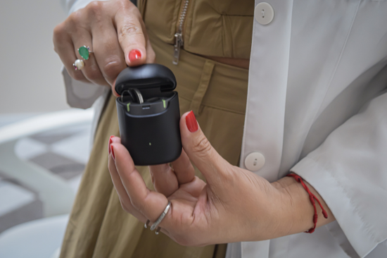 Profissional da saúde segurando estojo de carregamento com aparelho auditivo intra-auricular moderno.