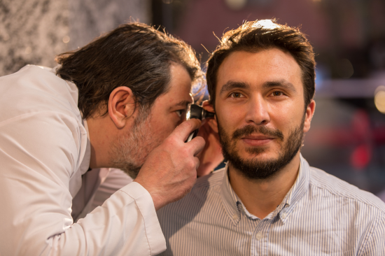 Como é feito o exame de audiometria - médico examinando ouvido de homem durante avaliação auditiva.