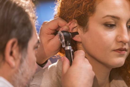 Médico realizando exame de ouvido em paciente para avaliação auditiva.